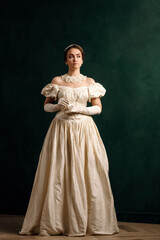 full-length portrait of a girl in a beige dress standing against a green wall