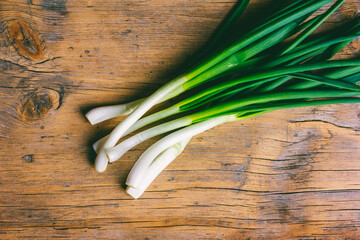 a bunch of young fresh green onions on a wooden background close-up with copy space