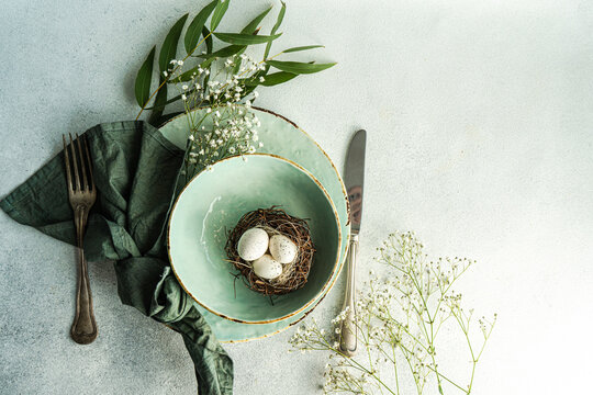 Overhead view of an Easter Place setting with Easter eggs in a bird's nest, ruscus branches and white Gypsophila flowers