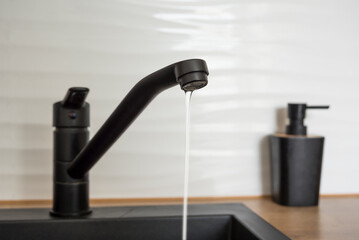 Black kitchen faucet with a little flowing water. Water shortage concept