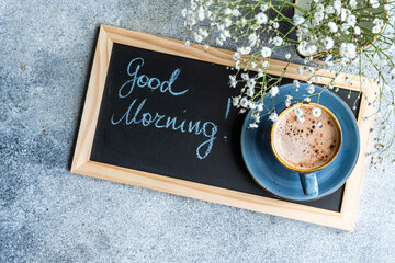 Overhead view of a bunch of white Gypsophila flowers and cappuccino next to a blackboard with the words good morning