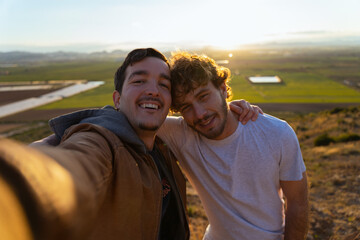 Selfie of two friends on top of a hill after a walk in the bush. They smile at the camera and rest their arm on each other's back. Concept of friendship and happiness