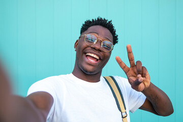 Selfie of cheerful handsome man in the street. Portarit of happy young man doing a selfie photo on the camera on a turquoise background wall.