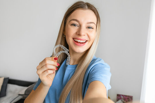 Female doctor holding a transparent dental aligner and make selfie, recommending this new treatment. Dental healthcare concept.