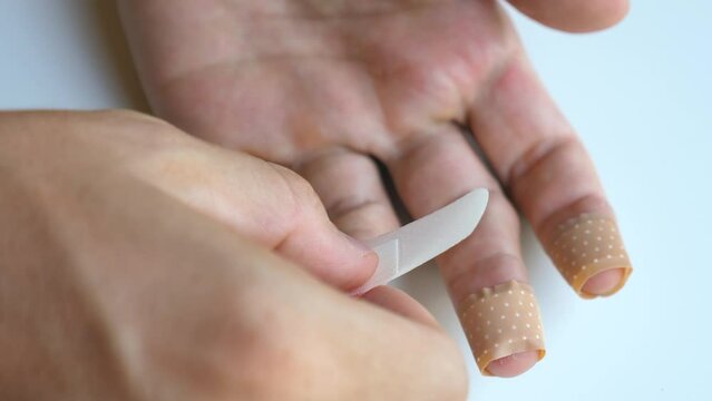 Man applying band aid patch on cuts wound on fingers. Male putting medical adhesive bandage tape sticking plaster to injured sore finger. First aid after accident, self cure help concept. Close-up