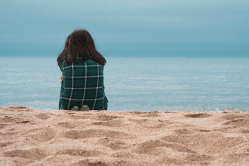 a dark hair girl/lady sitting on sand looking into horizon by the sea shore