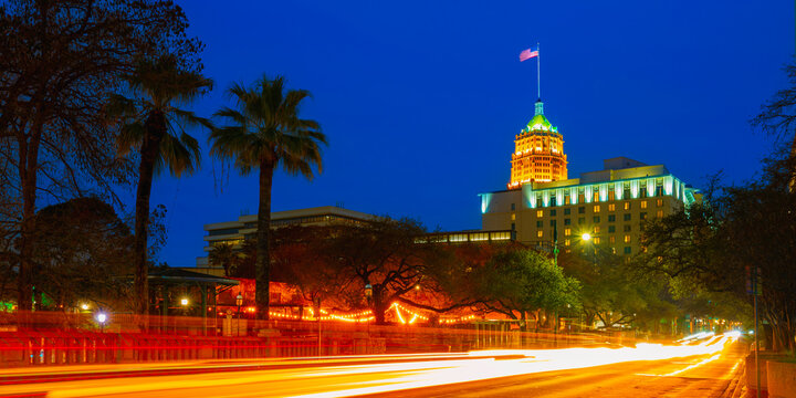 San Antonio Texas Night Street Landscape With Car Light Trails, Skyline Buildings, Waving American Flag, And Palm Trees In Winter