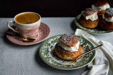 Homemade semlor buns with frangipane and whipped cream on vintage plate and cup of coffee on linen tablecloth.