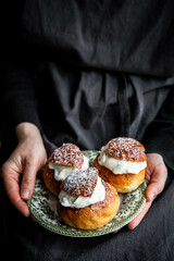Woman holding vintage plate with homemade semlor buns with frangipane and whipped cream.