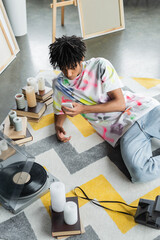 High angle view of african american artist using smartphone near record player and books in studio.