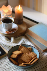 Fototapeta na wymiar Vintage books, reading glasses, e-reader, cup of tea, bowl of biscuits and lit candle on the table. Selective focus.