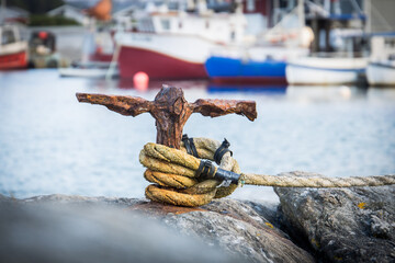 Rusty and weathered poller on a small harbour dock with a yellow rope around it