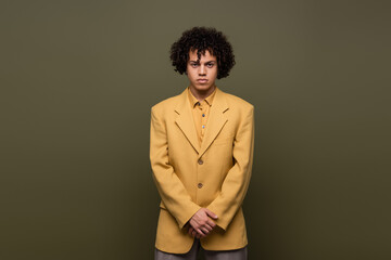 front view of young african american man with curly hair posing in yellow blazer on grey background