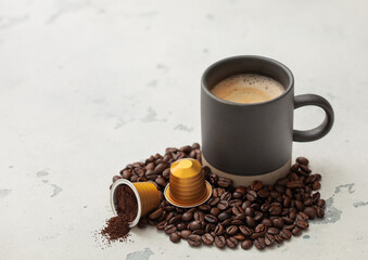 Coffee cup with fresh beans and ground coffee capsules on light kitchen background.