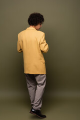 Fototapeta premium back view of young african american man in yellow blazer and trousers on grey green background
