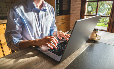 Businessman writing on his laptop in his office with a coffee cup, stylus in hand and tablet nearby. Young entrepreneur working remotely on his computer at home