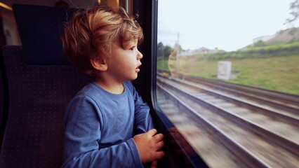 Child travels by train looking outside through window glass