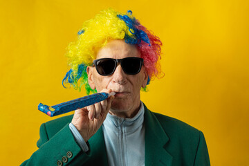 Front view of an old man dressed for carnival with sunglasses, green jacket, colored wig and carnival trumpet