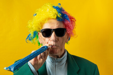 Old man dressed for carnival with sunglasses, green jacket, colored wig and carnival trumpet