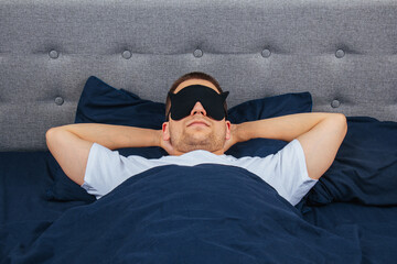 Top view high angle photo of young man wearing sleep mask, happy positive smile, sleep blanket, blanket, clothes, pajamas.