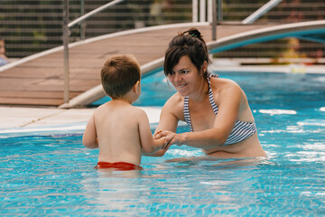 Mom teaches a little boy to swim in the pool.