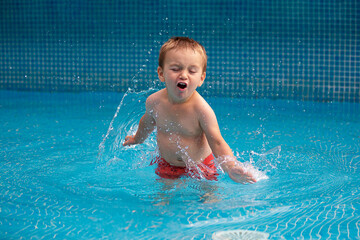 Happy little boy is playing with water in the pool.