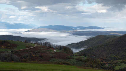 Mountain landscape with valley filled with fog and cloudy sky in morning, autumn season in mountains