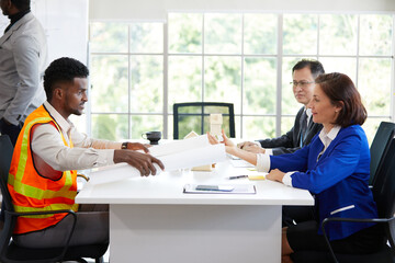 engineer holding white paper or blueprint and talking with colleagues in the office