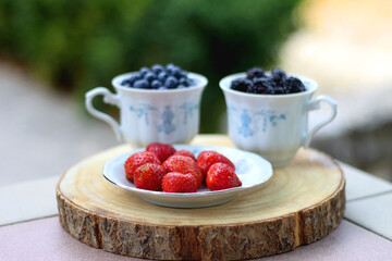 Blueberries, blackberries and strawberries in the vintage porcelain set. Healthy snack served in a garden. Selective focus.