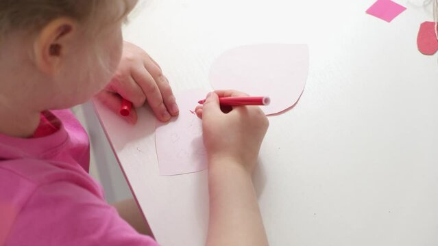 cute girl with blond curly hair signs a card in the shape of a heart