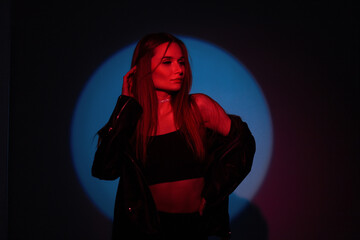 Beautiful young stylish girl in fashion black clothes on a dark blue background with creative red light