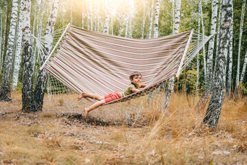 Cute little boy lying on big hammock in birch grove. Child smiling, camping life
