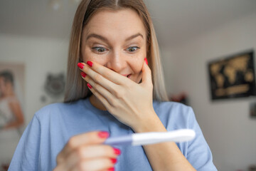 Happy smiling woman looking at pregnancy test at home. Pregnancy, fertility, maternity, emotions and people concept . © Ivan