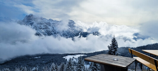 Panoramic view of snowy mountains in Italy, with mountains showing through clouds and snowy trees.