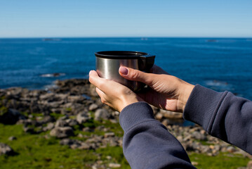 Woman with a cup of hot tea and a thermos sits on the ocean and admires the picturesque landscape. Beautiful nature. Harmony, relaxed lifestyle. Travel, adventure. Explore Northern Norway. Scandinavia