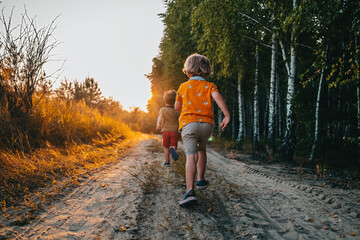 Obraz premium Cute kids, boys runs at summer nature road. Brothers, playing outdoors. Sunset.