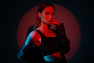 Fototapeta na wymiar Cool hight fashion female studio portrait of a beautiful stylish woman in trendy black rock clothes with red color light on a dark background