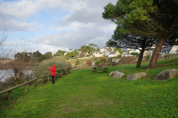 Fototapeta na wymiar Kid with red raincoat taking a picture in a garden above the beach, Lancieux, Brittany
