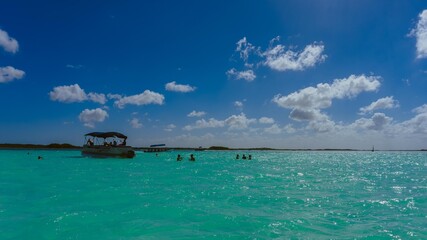 Fototapeta na wymiar Fotografia de paisaje en la laguna de Bacalar con gente nadando y un pequeño bote al fondo