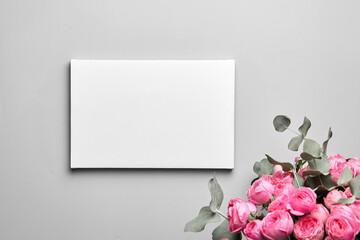 White canvas mockup hanging on grey wall and bouquet of pink roses with eucalyptus leaves. Blank canvas, interior decor