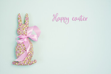 Happy easter. Decorative handmade Easter Bunny soft toy made of cotton fabric, decorated with pink satin ribbon. Isolated on blue background. Mockup for greeting card. Space for text. top view