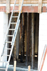 A ladder leaning against a wall, a rough window opening, reinforced brick lintels, walls made of autoclaved aerated concrete and wooden building props inside a house under construction