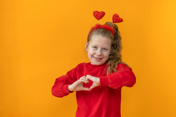 cute joyful baby girl in a red sweater with a red heart in her hands on an isolated yellow background valentine's day concept. High quality photo