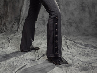 A man in elegant trousers with buttons, close-up. Portrait in the studio on a gray fabric background
