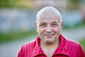 Grinning bald man in his 60s with an unshaven face.
