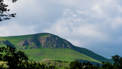Rocky hill with grass on the surface, huge white clouds over the top , laconic landscape