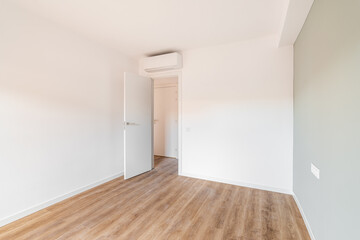 Bright spacious bedroom with parquet flooring. An open door from the room leading to a corridor with other rooms. Air conditioning above the door saves from summer heat