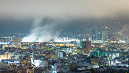 Fototapeta premium Cityscape of Graz at night with buildings and smoking plants in far distance