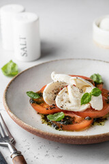 Caprese salad in modern feed with tomatoes, basil, mozzarella, pesto. Traditional Italian food with cutlery on white background, menu
