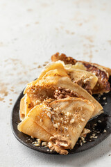 Crepes with honey or syrup and nuts on brown plate on beige textured background with copy space. Pancake day or Maslenitsa traditional food concept